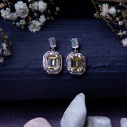 A pair of exquisite yellow gemstone earrings displayed on a textured background with floral accents and a crystal.