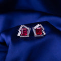 A pair of sterling silver earrings with a red stone set in a geometric pattern, displayed on a blue textured surface.