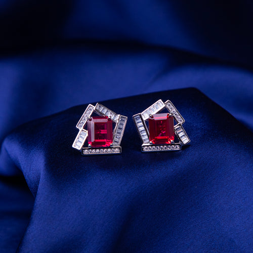 A pair of sterling silver earrings with a red stone set in a geometric pattern, displayed on a blue textured surface.