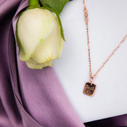 A sterling silver pendant chain with a rose gold color, featuring a smiley face design, displayed on a purple fabric background with a flower and a petal.