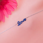 A sterling silver bracelet with the word 'Love' written in blue letters, displayed against a pink background with a pink flower.
