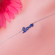 A sterling silver bracelet with the word 'Love' written in blue letters, displayed against a pink background with a pink flower.