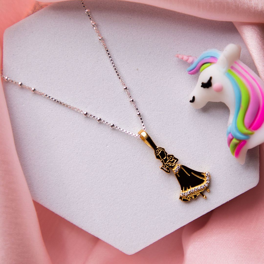 A silver and golden pendant chain necklace with a shoe-shaped pendant, displayed on a pink fabric next to a multicolored unicorn figurine.