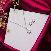 A sterling silver star pendant necklace and a pair of earrings, displayed on a white card with a pink satin backdrop and small white flowers.
