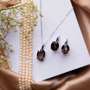 A set of sterling silver jewelry including a pendant and a pair of earrings with brown stone pendants, displayed on a white surface with a floral background.