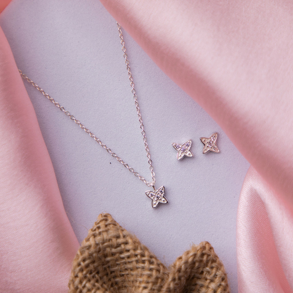 A silver pendant set with a butterfly motif and accompanying earrings, displayed on a pink fabric surface.