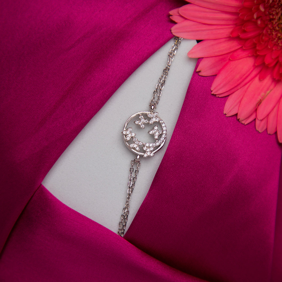 A sterling silver charm bracelet with a butterfly design, displayed on a pink fabric surface.