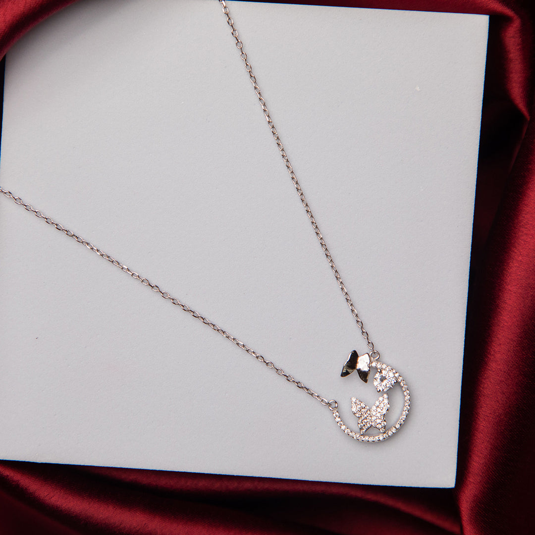 A silver pendant chain necklace with a motif of three butterflies, two of which are embellished with white stones, displayed against a white and red background.
