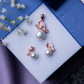 A rose gold-finish silver pendant set featuring a butterfly motif on a pearl, accompanied by matching earrings, displayed on a blue surface with white flowers.