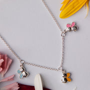 A silver pendant chain necklace with various bee designs, displayed against a backdrop of flowers.