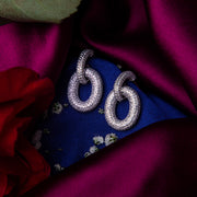 A pair of chunky silver bedazzled link earrings displayed against a purple fabric backdrop with a floral pattern and a red rose beside it.