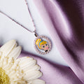 A silver pendant chain featuring a portait of Cinderella with a radiant smile, placed on a white flower against a purple backdrop.