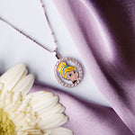 A silver pendant chain featuring a portait of Cinderella with a radiant smile, placed on a white flower against a purple backdrop.