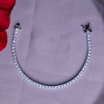 A silver tennis bracelet with a clasp, displayed on a grey surface with a red cloth in the background.