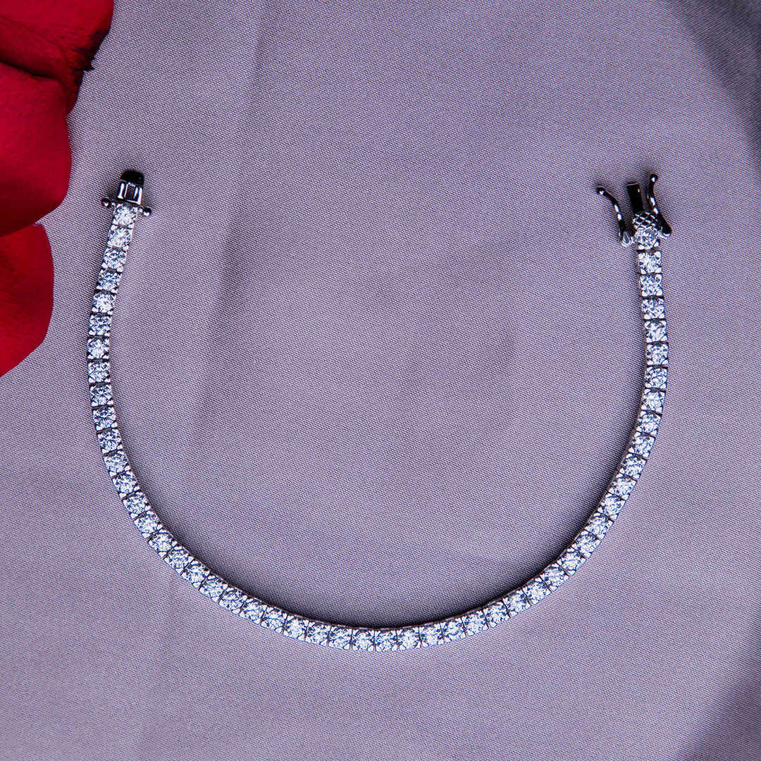 A silver tennis bracelet with a clasp, displayed on a grey surface with a red cloth in the background.
