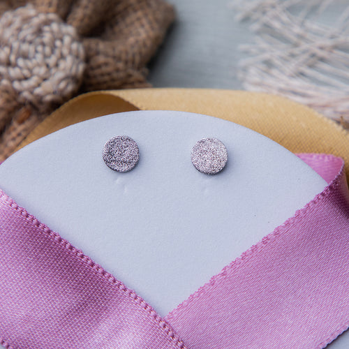 A pair of silver textured stud earrings displayed on a pink fabric surface.