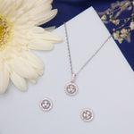A sterling silver pendant set with a round embellished center pendant and a pair of matching earrings, displayed on a white surface with a flower and a blue background.