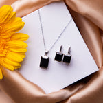 A black stone pendant set with a necklace and earrings, displayed on a white card with a yellow flower on the side.