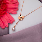 A rose gold finish pendant chain featuring a clover-shaped design with a suspended pearl, displayed against a floral background.