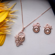 A rose gold pendant set with a floral design on a chain and a pair of matching earrings, displayed on a surface with some flower petals scattered around.