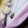 A sterling silver pendant chain featuring a monkey motif, displayed alongside a white flower on a purple fabric background.