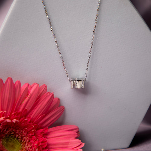 A sterling silver pendant chain displayed on a mannequin with a pink flower beside it.
