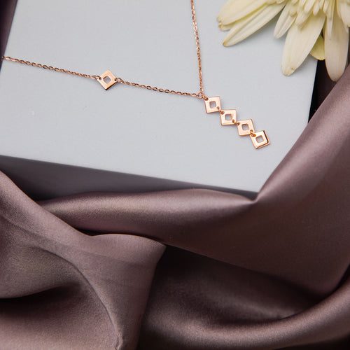 A rose gold-colored everyday pendant chain with interconnected cubes, displayed on a soft fabric surface.