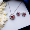 A set of jewelry featuring a dazzling pink stone pendant and a pair of earrings, placed on a white surface next to a white flower.