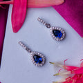 A pair of sterling silver drop earrings with deep blue gemstones and white accents, displayed on a surface with pink and blue floral accents.