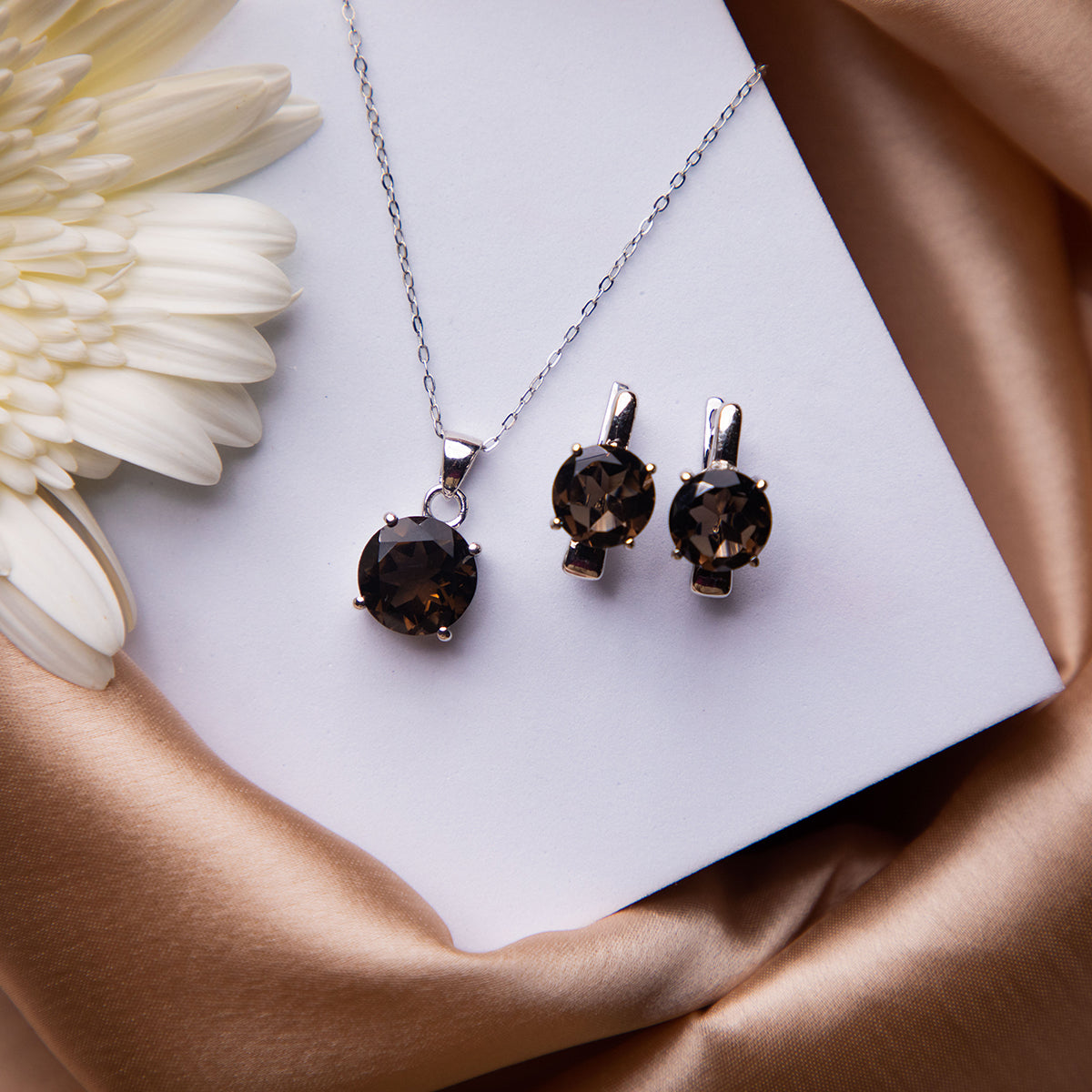 A set of jewelry featuring a deep brown stone pendant and a pair of earrings, displayed on a white card with a satin background.