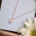 A silver-colored cubic pendant chain with intricate details, presented on a white background with a flower beside it.