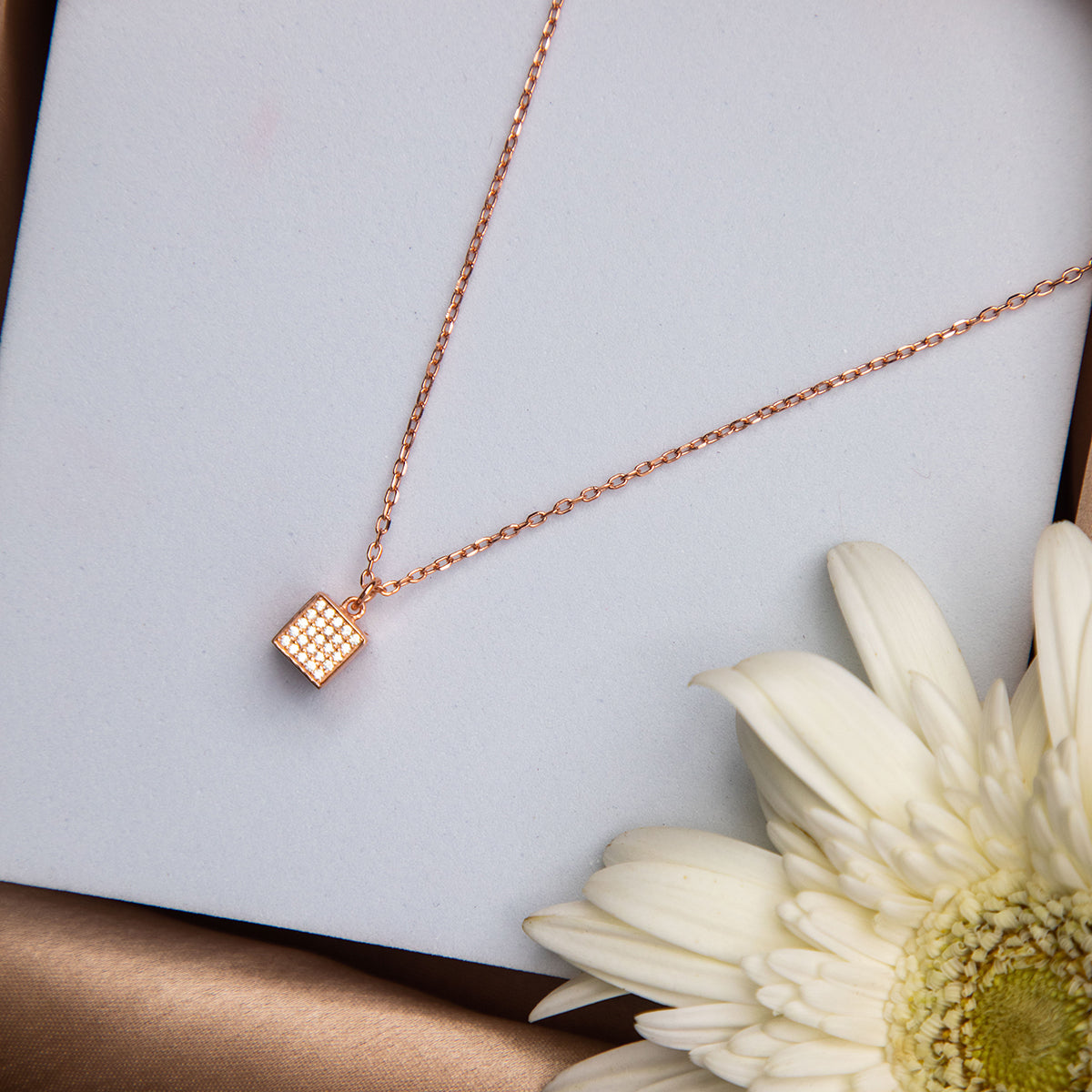 A silver-colored cubic pendant chain with intricate details, presented on a white background with a flower beside it.