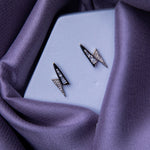 A pair of silver embellished earrings with a geometric design, displayed on a purple fabric surface.