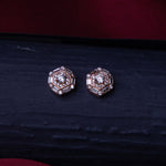 A pair of rose gold-colored sterling silver stud earrings with a halo design and a central brilliant stone, placed on a dark surface.