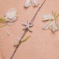 A silver bracelet featuring an embellished starfish charm, displayed on a pink background with scattered white flowers.