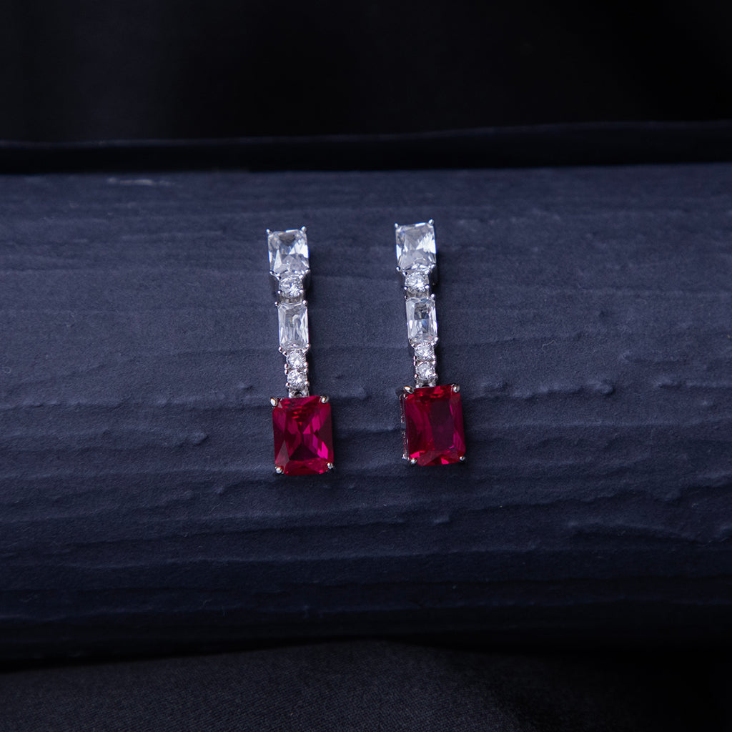 A pair of emerald-cut red stone earrings with a silver rhodium-based anti-tarnish coating, displayed against a dark background.
