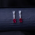 A pair of emerald-cut red stone earrings with a silver rhodium-based anti-tarnish coating, displayed against a dark background.