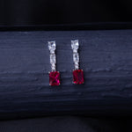 A pair of emerald-cut red stone earrings with a silver rhodium-based anti-tarnish coating, displayed against a dark background.