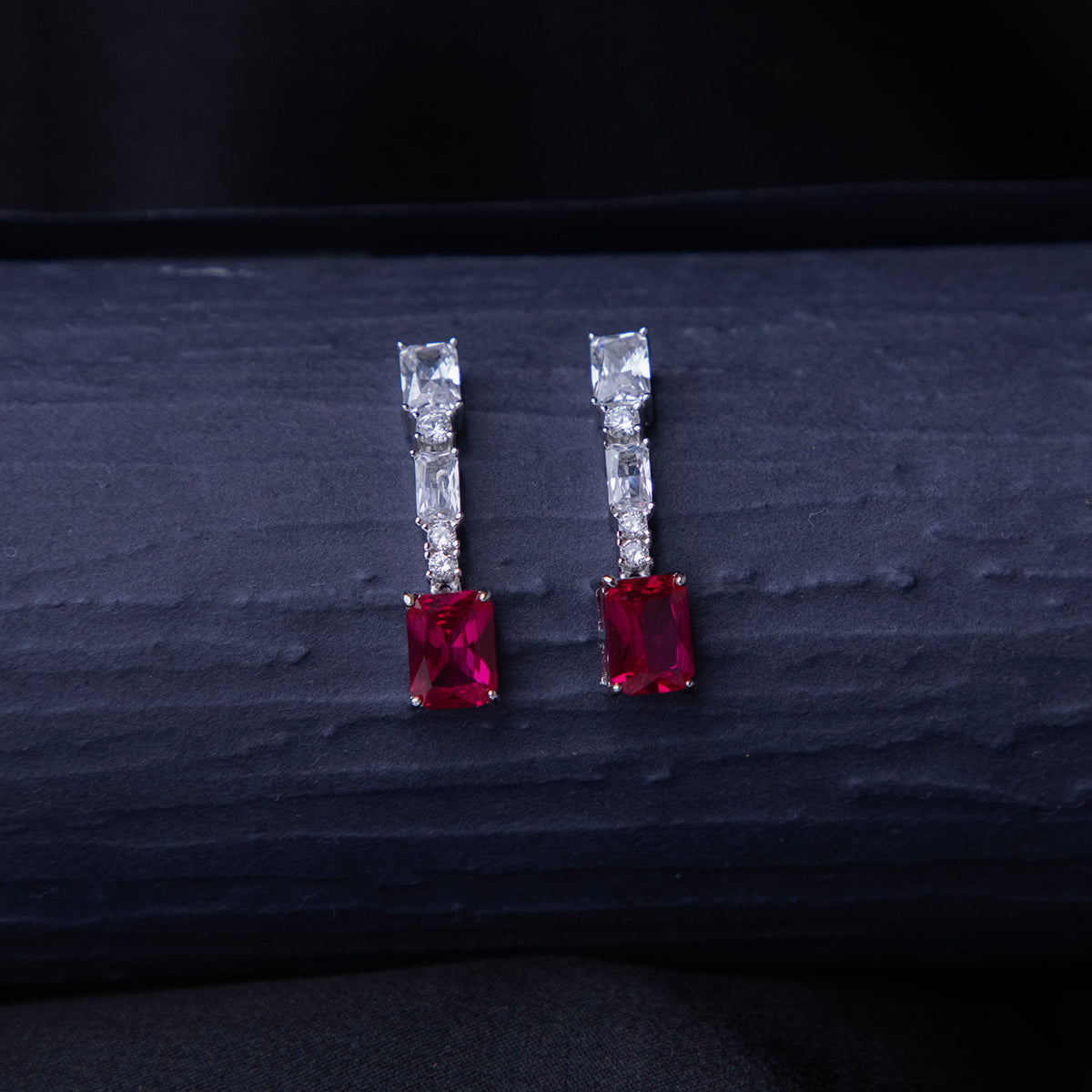 A pair of emerald-cut red stone earrings with a silver rhodium-based anti-tarnish coating, displayed against a dark background.
