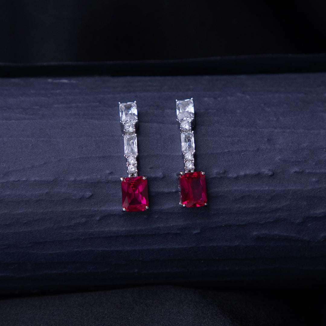 A pair of emerald-cut red stone earrings with a silver rhodium-based anti-tarnish coating, displayed against a dark background.