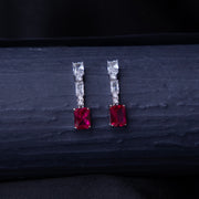 A pair of emerald-cut red stone earrings with a silver rhodium-based anti-tarnish coating, displayed against a dark background.