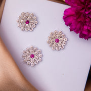 A set of sterling silver daisy-shaped pendants with pink centers, displayed on a flat surface with a flower and a book in the background.