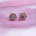 A pair of rose gold-colored evening primrose stud earrings displayed against a pink background.
