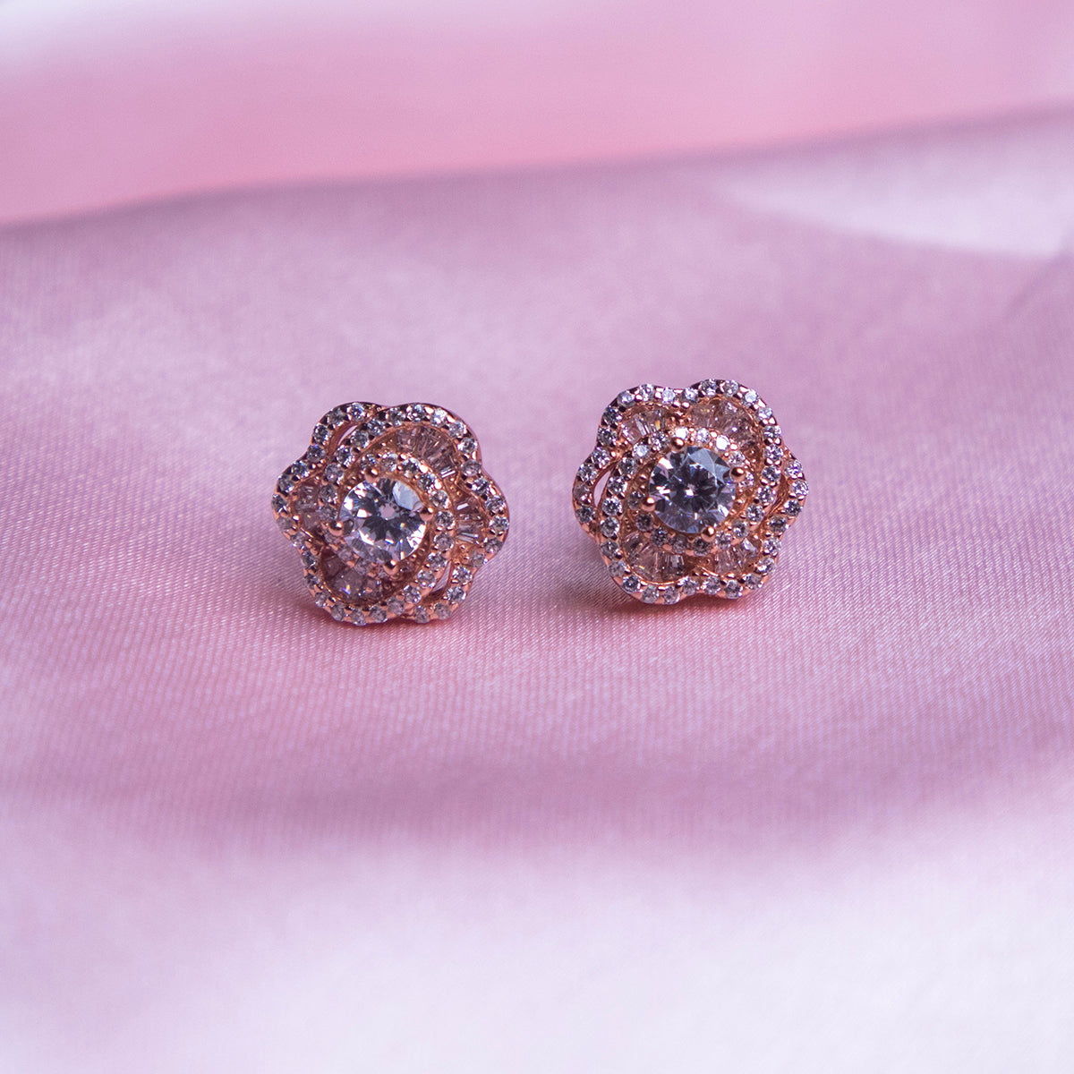 A pair of rose gold-colored evening primrose stud earrings displayed against a pink background.