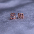 A pair of rose gold-finish stud earrings with a rhodium-based anti-tarnish coating on a textured background.