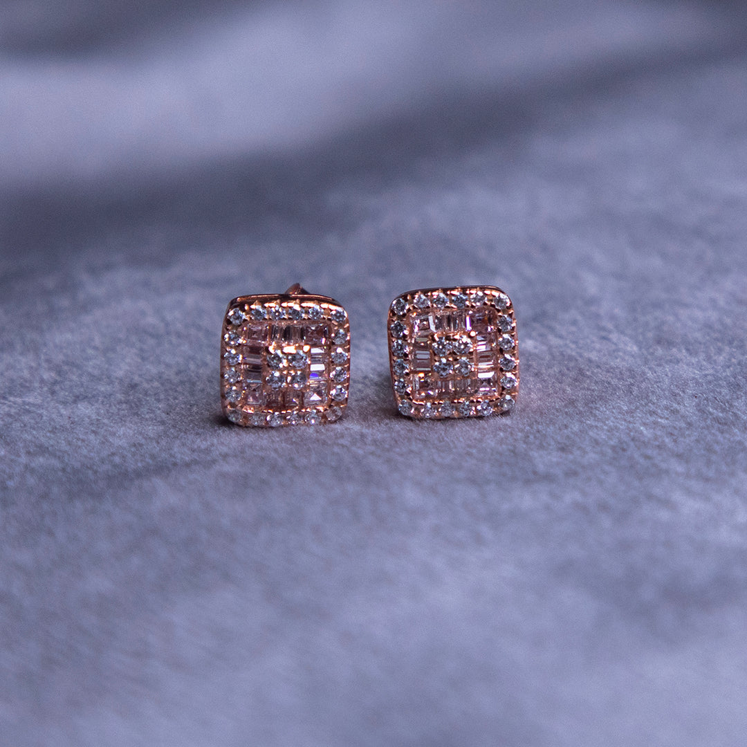 A pair of rose gold-finish stud earrings with a rhodium-based anti-tarnish coating on a textured background.