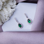A pair of sterling silver drop earrings with green gemstones, displayed on a white surface with a floral background.