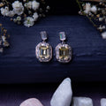 A pair of exquisite yellow gemstone earrings displayed on a textured background with floral accents and a crystal.