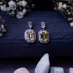 A pair of exquisite yellow gemstone earrings displayed on a textured background with floral accents and a crystal.