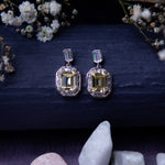 A pair of exquisite yellow gemstone earrings displayed on a textured background with floral accents and a crystal.